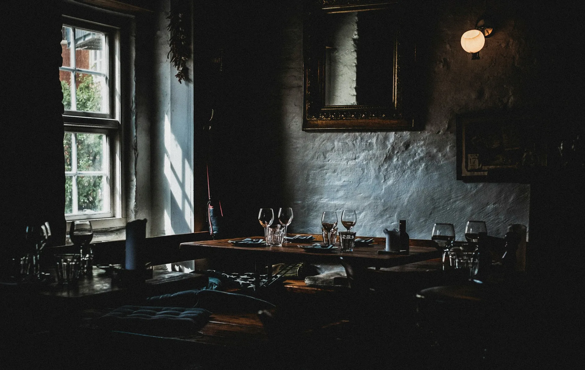Loş ışıklı restoran salonunda pencere kenarında kurulmuş masa ve bardaklar