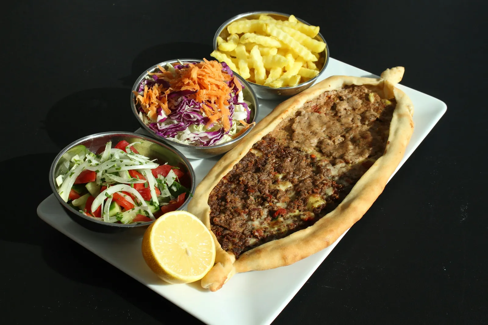 Beyaz tabakta kıymalı pide, salata ve kızarmış patates